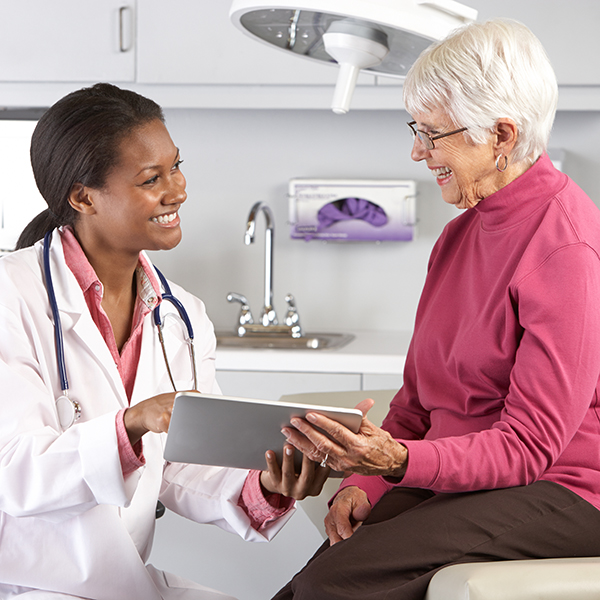 Doctor Discussing Records With Senior Female Patient Smiling